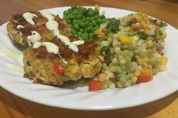 A plateful of food, including two lake trout cakes with dipping sauce, green peas, and couscous salad.