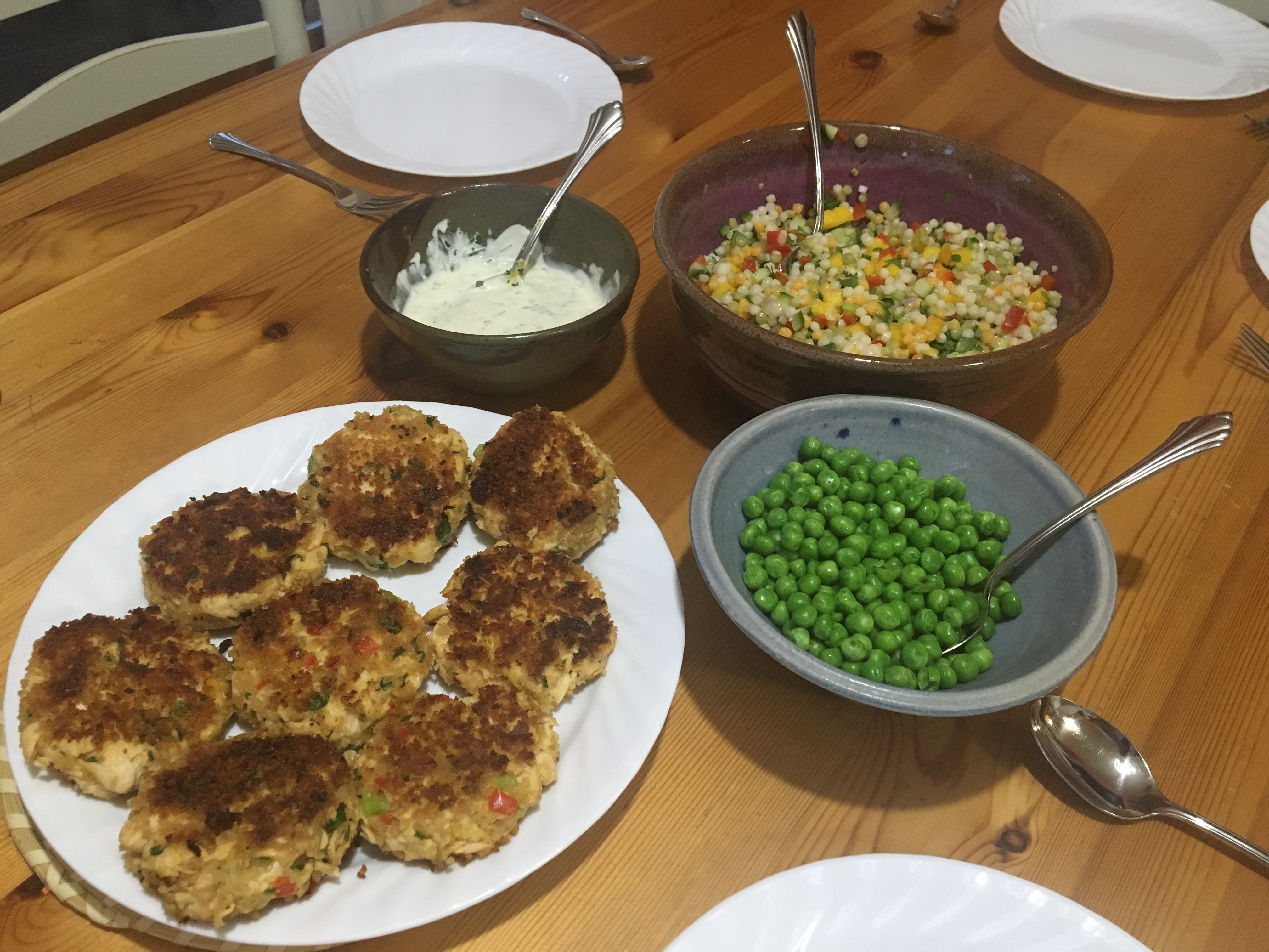 Wooden table with fried lake trout cakes, green peas, mango couscous salad, and dipping sauce