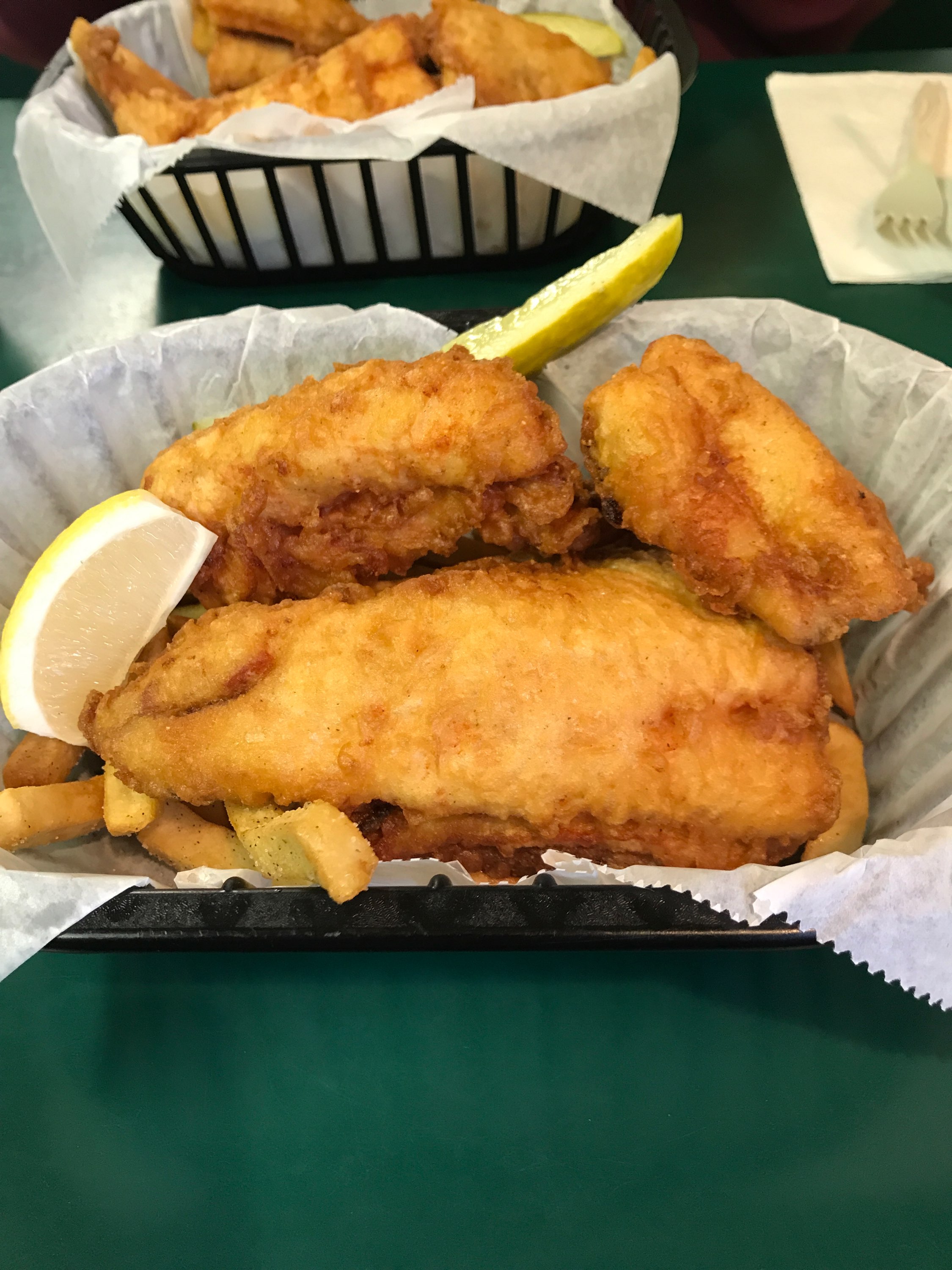 Basket of fried whitefish with lemon wedge and pickle.