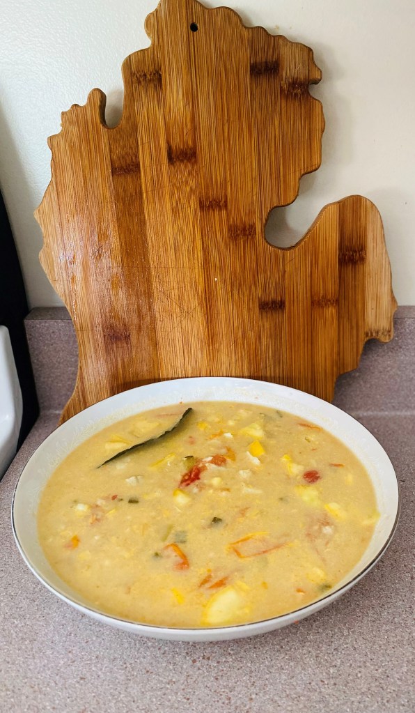 Large bowl of coconut curry with bluegill in front of a cutting board shaped like Michigan’s lower peninsula. Photo by A. Rodriguez Cole