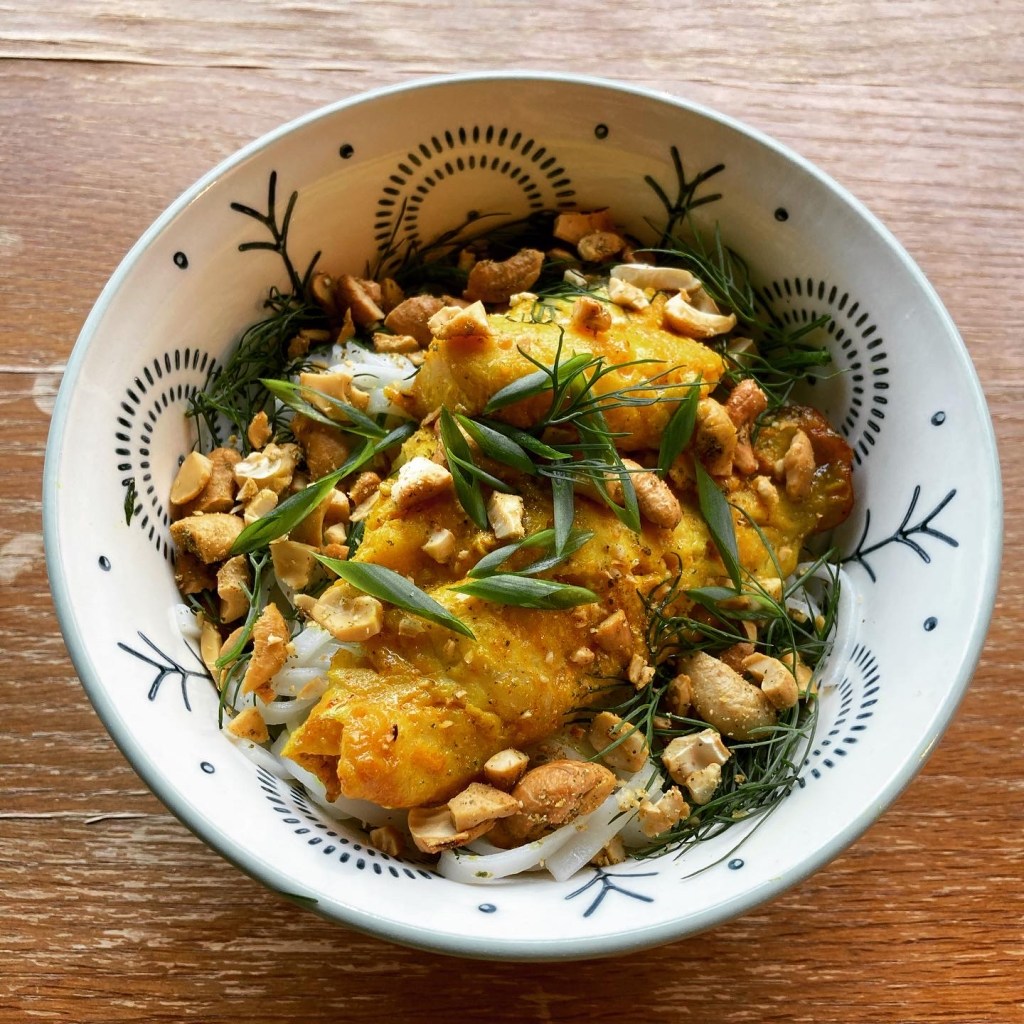 A bowl of turmeric-marinated fish with mixed herbs, served over rice noodles. Photo by El Lower