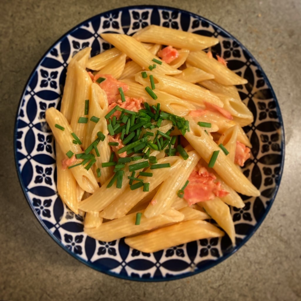 A bowl of penne pasta with a creamy sauce, flakes of smoked salmon, and chopped chives.