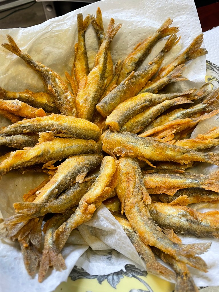 A pile of small fish, battered and deep-fried, on a piece of paper towel.