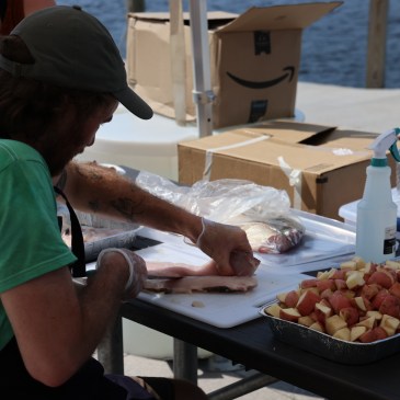 A man leans over a table with a fillet of fish next to a pile of chopped potatoes