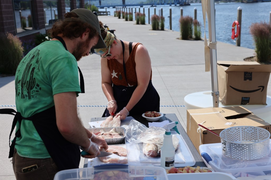 Evan and Alex stand over a table full of potatoes and fish fillets, preparing their fish boil.