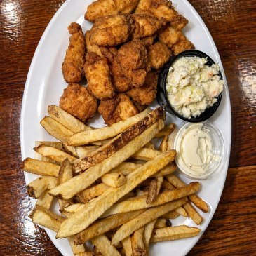 An oval plate containing fried fish, potato fries, and side sauce