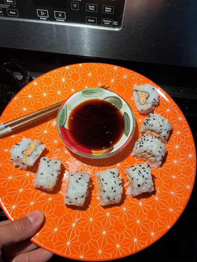 Eight rounds of sushi sit on an orange plate with a bowl of tamari dipping sauce